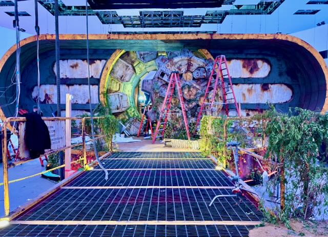 Sci-fi portal set — distressed metal arch ringed by ladders and overgrowth, scenic build mid-install.