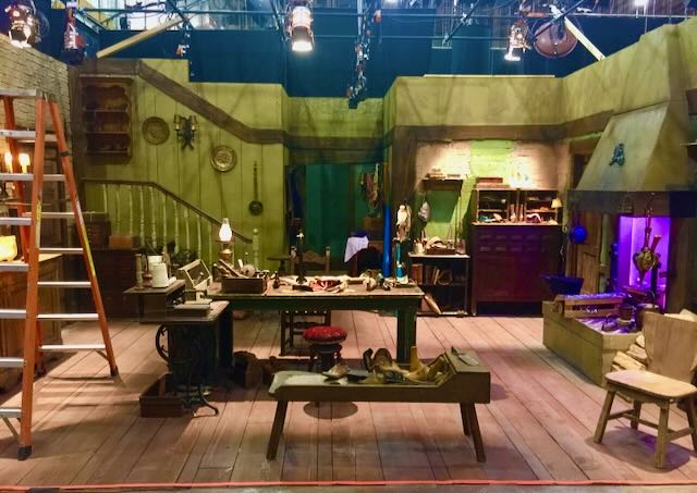 Period cobbler's workshop set lit by hot tungsten with a touch of green UV spill on the back wall.