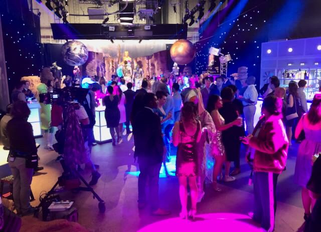 Gala under a starcloth ceiling, planet props and disco-ball moons lit in hot pink and electric blue while guests mingle.
