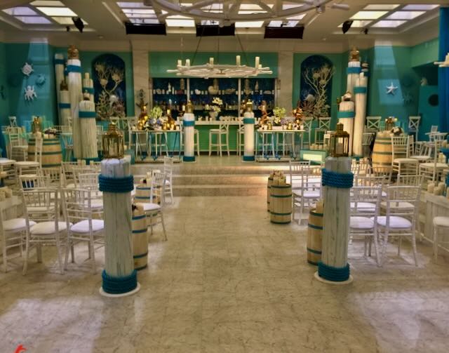 Nautical-themed event build — rope-wrapped columns, lanterns, white-and-teal palette around a candlelit bar.
