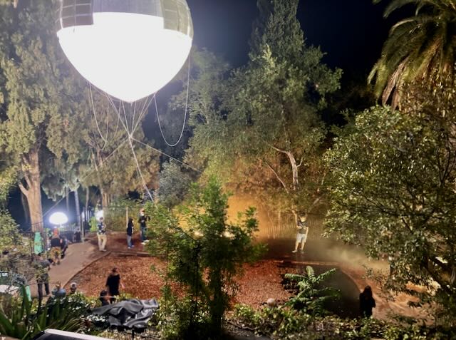 Night exterior film shoot — balloon light hovering over a wooded path while crew works the scene below.